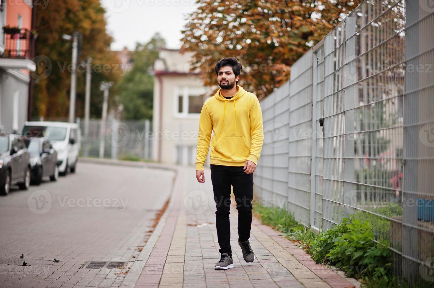 homem indiano urbano jovem hippie em um moletom amarelo na moda. cara legal do sul da Ásia usa capuz andando na rua de outono. foto