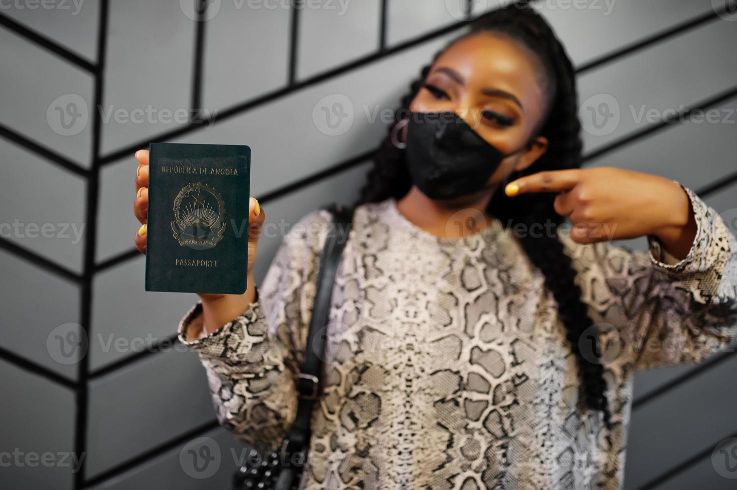 mulher africana usando máscara facial preta mostra passaporte angola na mão. coronavírus no país africano, fechamento e quarentena de fronteiras, conceito de surto de vírus. foto