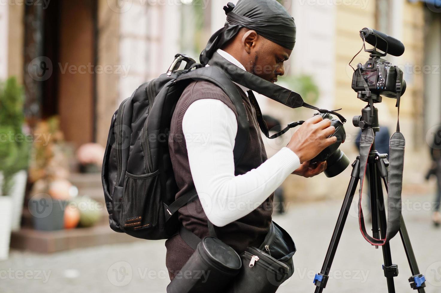 jovem cinegrafista americano africano profissional segurando a câmera profissional com equipamento pro tripé. cinegrafista afro vestindo duraq preto fazendo vídeos. foto