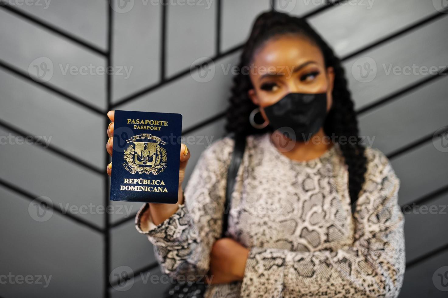 mulher afro-americana usando máscara facial preta mostra passaporte da república dominicana na mão. coronavírus no país da américa, fechamento de fronteiras e quarentena, conceito de surto de vírus. foto