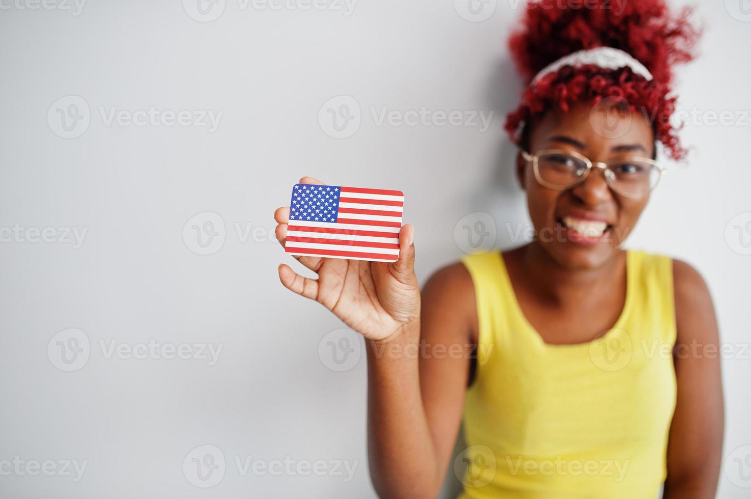 mulher afro-americana com cabelo afro, use camiseta amarela e óculos, segure a bandeira dos eua isolada no fundo branco. foto