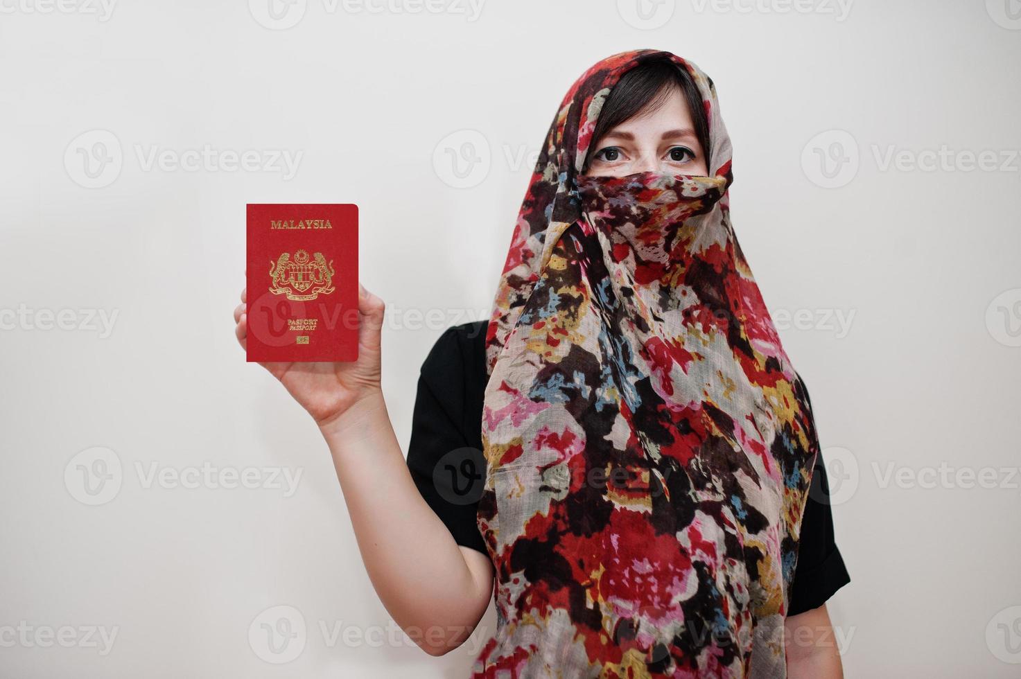 jovem muçulmana árabe em roupas hijab segura passaporte da malásia no fundo da parede branca, retrato de estúdio. foto