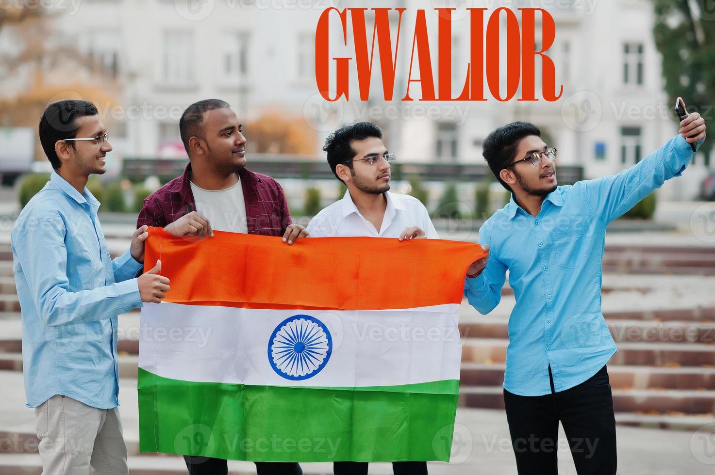 inscrição da cidade de gwalior. grupo de quatro amigos indianos do sexo masculino com bandeira da índia fazendo selfie no celular. maior conceito de cidades da índia. foto