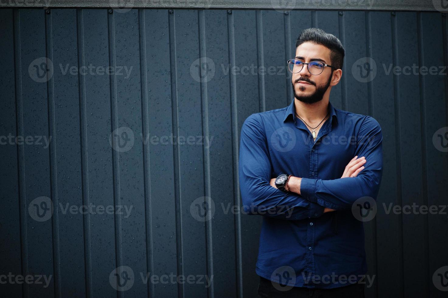 empresário do Oriente Médio usa camisa azul, óculos, contra a parede de aço. foto