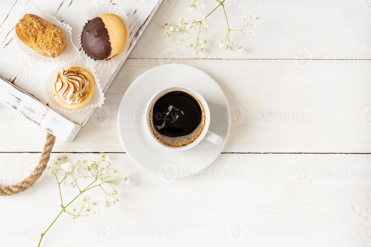 vista superior da xícara de café preto e mini bolos em uma bandeja de madeira com espaço de cópia. composição do café da manhã foto