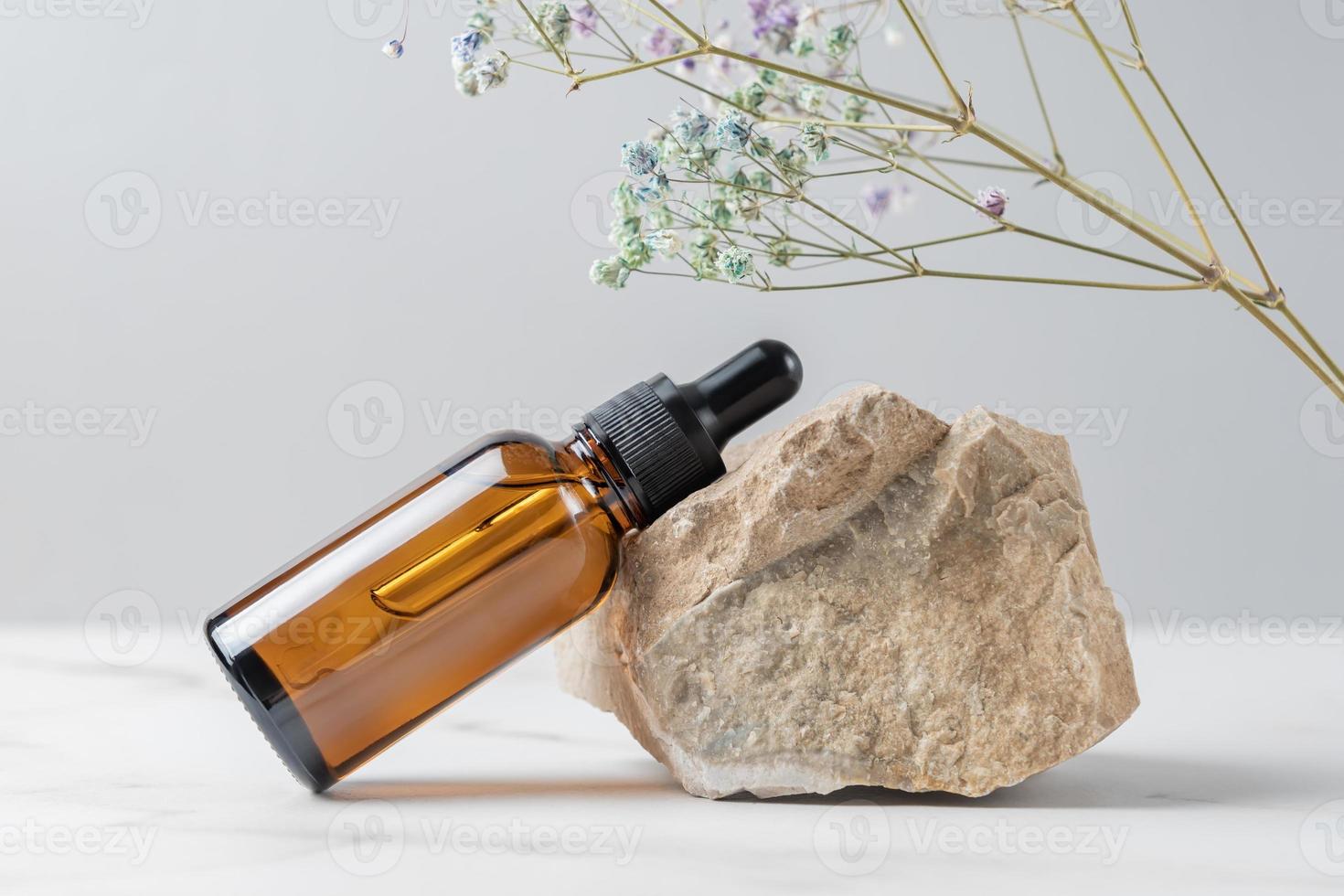 soro facial ou óleo essencial em frasco conta-gotas de vidro escuro perto da pedra e ramo seco da flor gypsophila. cosmético para a pele. conceito de apresentação do produto foto