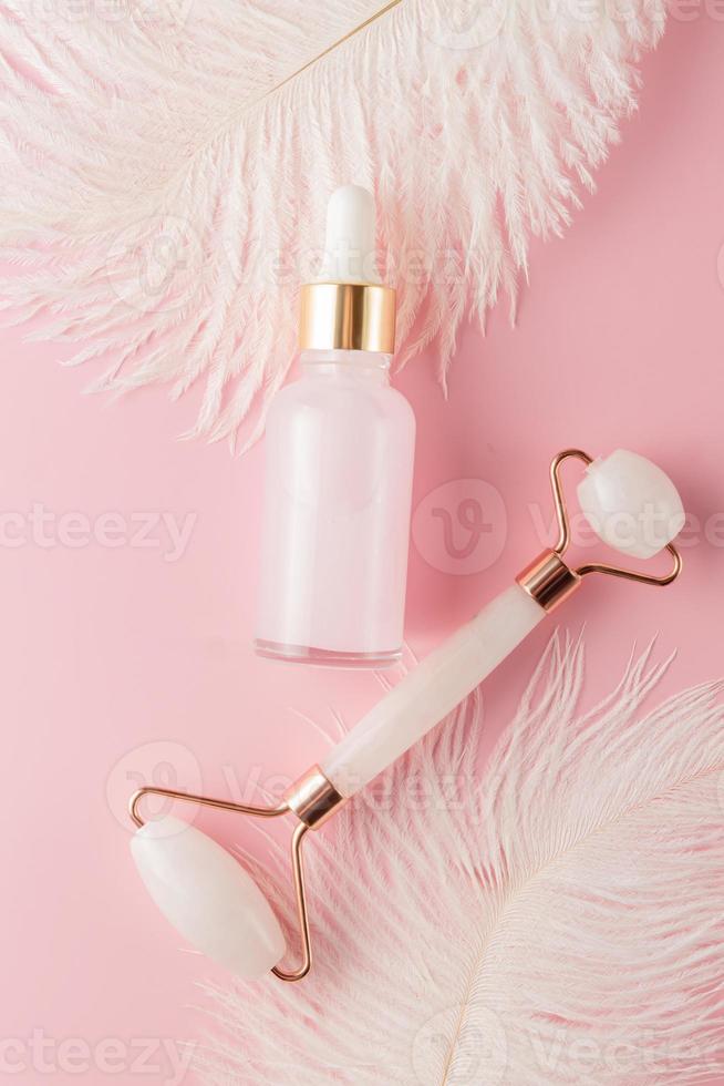 conjunto cosmético de spa em casa. rolo de quartzo rosa para massagear rosto e corpo e óleo de beleza natural com penas brancas macias foto