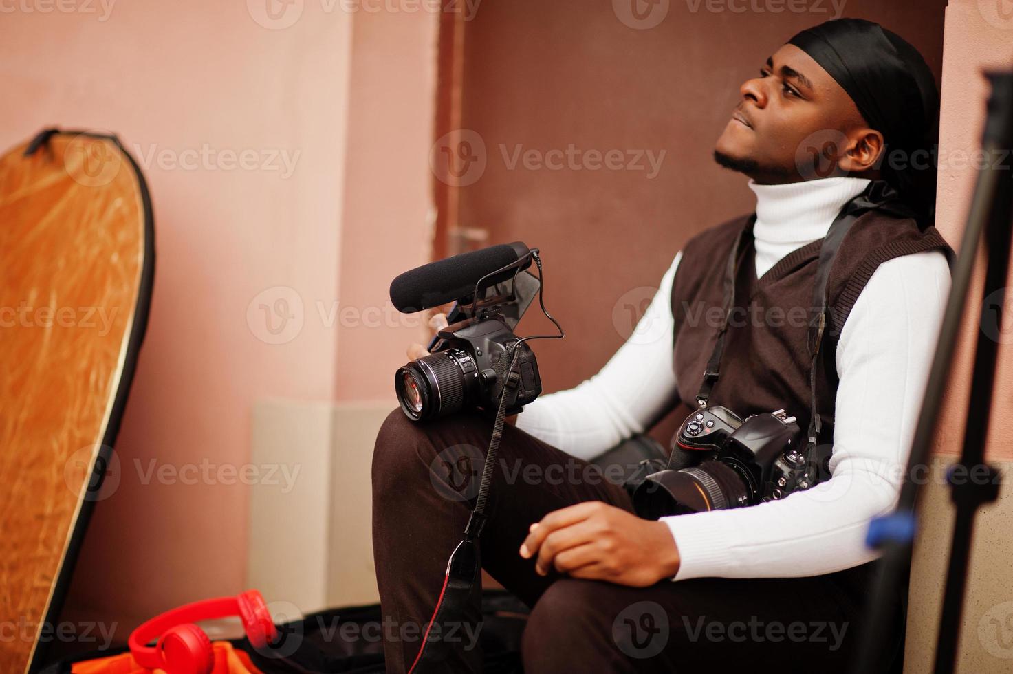 jovem cinegrafista americano africano profissional segurando câmera profissional com equipamento profissional. cinegrafista afro vestindo duraq preto fazendo vídeos. foto