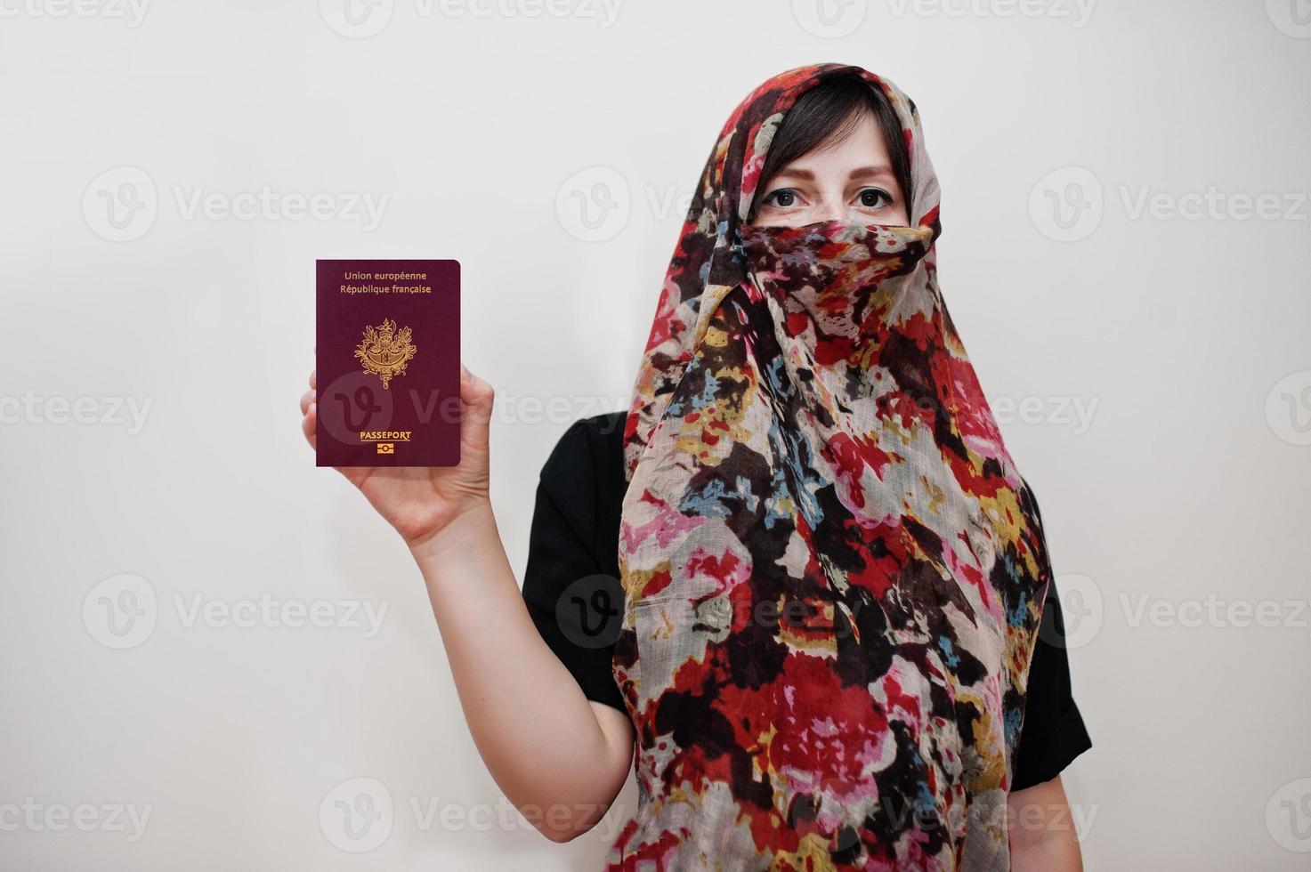 jovem muçulmana árabe em roupas hijab segura passaporte da república francesa no fundo da parede branca, retrato de estúdio. foto