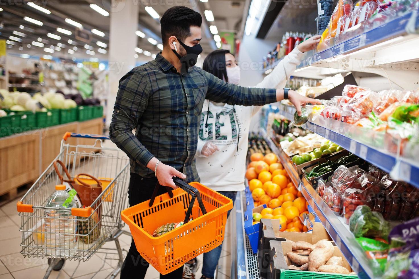 casal asiático usa máscara protetora fazendo compras juntos no supermercado durante a pandemia. tirando legumes da geladeira. foto
