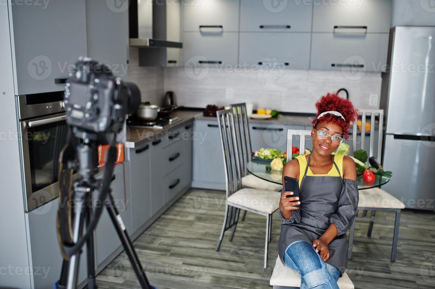 mulher afro-americana filmando sua transmissão de blog sobre comida saudável na cozinha de casa e olhando para o telefone. foto