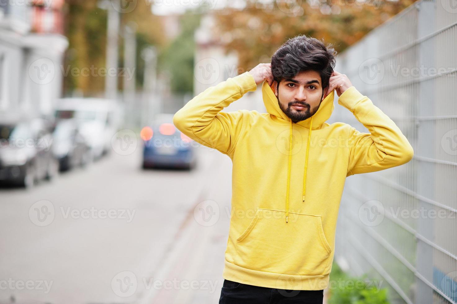 homem indiano urbano jovem hippie em um moletom amarelo na moda. cara legal do sul da Ásia usa capuz andando na rua de outono. foto