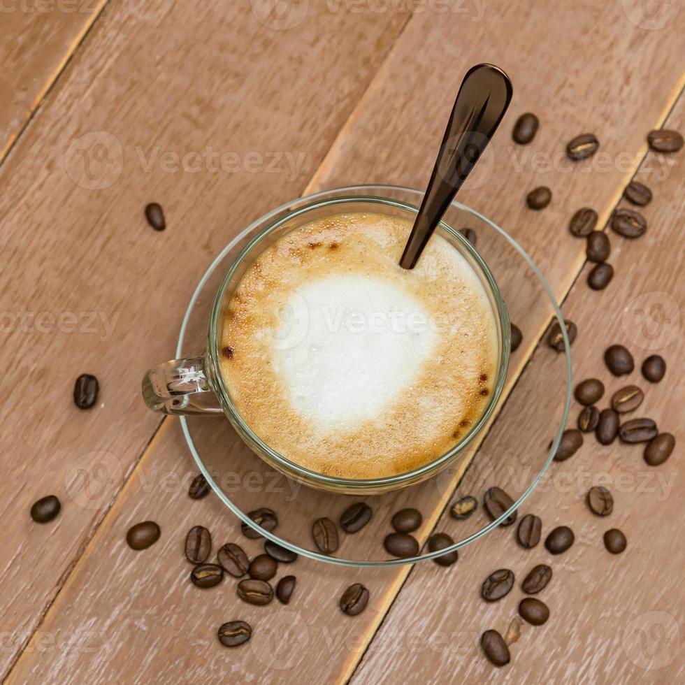 vista superior da xícara de café com leite quente ou cappuccino em um copo de vidro na mesa de madeira. café com espuma de leite com espaço de cópia foto