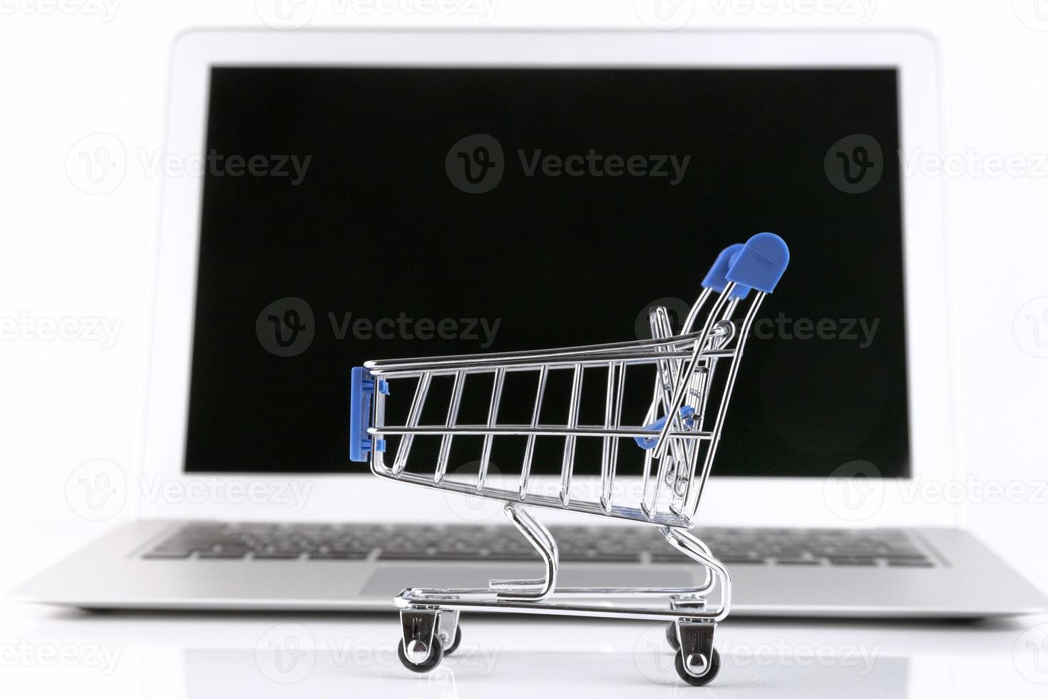 laptop com um pequeno carrinho de compras, em um fundo branco. foco seletivo. copie o espaço. foto