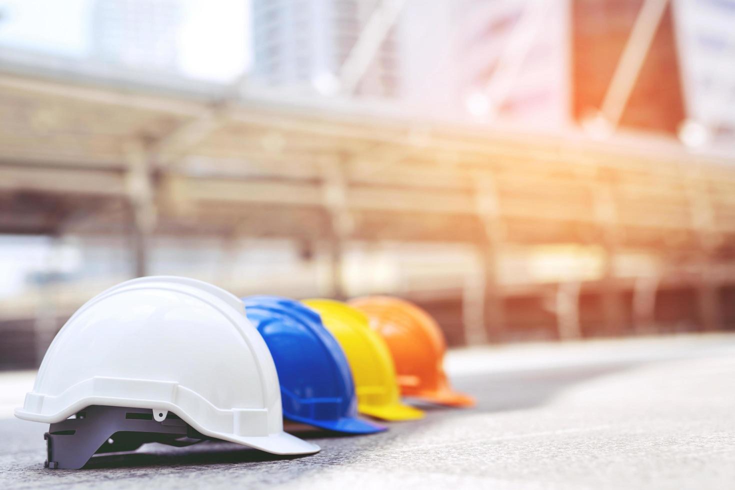 laranja, amarelo, azul e branco de segurança dura usar chapéu de capacete no projeto no edifício do canteiro de obras no piso de concreto na cidade. capacete para trabalhador como engenheiro ou trabalhador. conceito de segurança em primeiro lugar foto