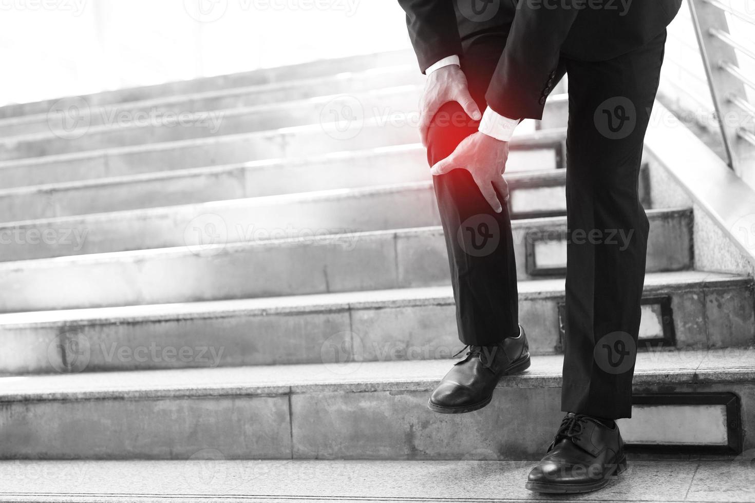 empresário de terno tem a dor dolorida e a expressão dolorosa do problema no joelho e anda para cima e para baixo na escada durante o escritório. conceito de cuidados de saúde. foto