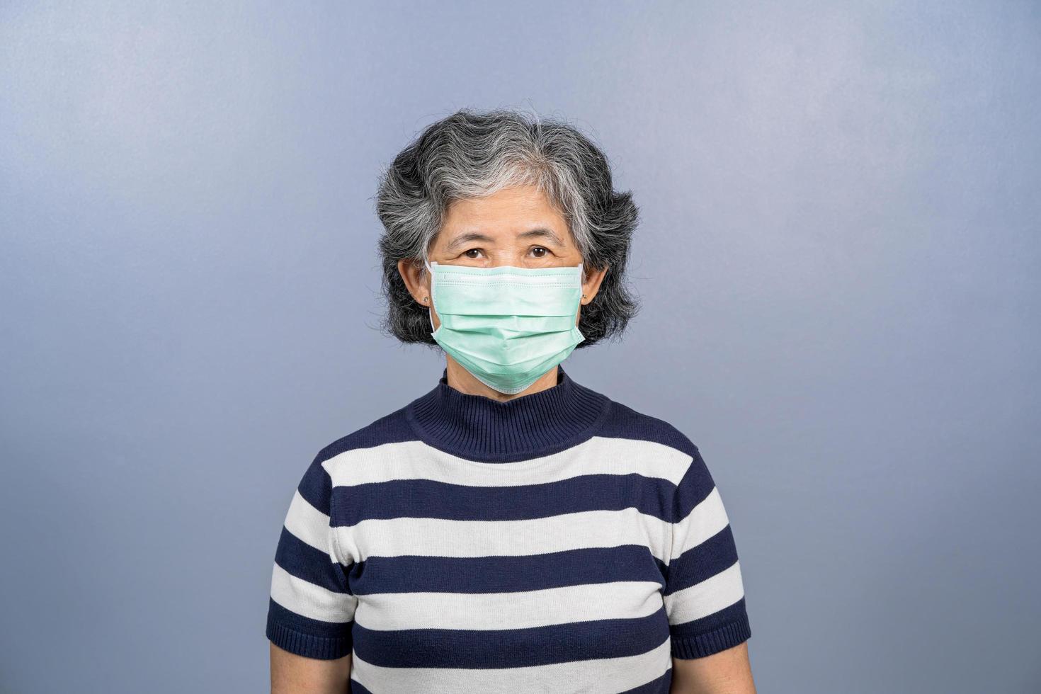 uma idosa asiática usando máscara cirúrgica em fundo sólido foto