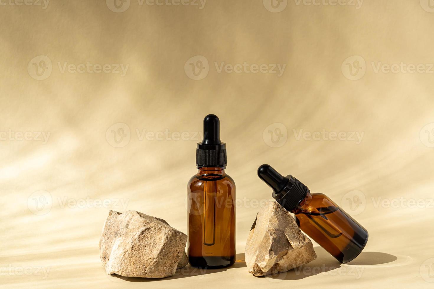 frascos de cosméticos de vidro escuro com um conta-gotas em um fundo bege com pedras e folhas tropicais. conceito de cosméticos naturais, óleo essencial natural e produtos para cuidados com a pele foto