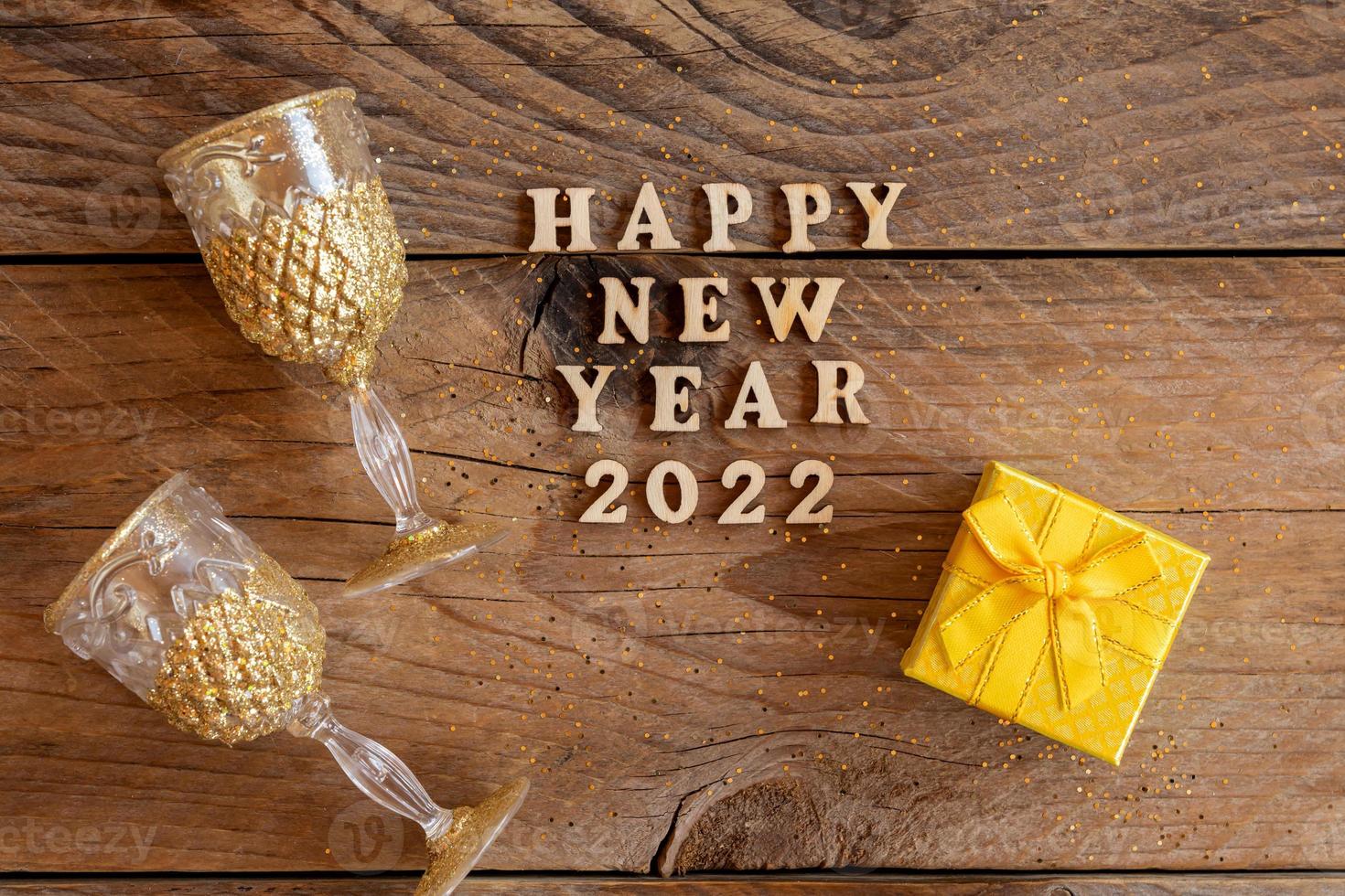 presentes de ano novo e taças de champanhe na mesa de madeira. texto feliz ano novo 2022. cartão festivo. postura plana. foto