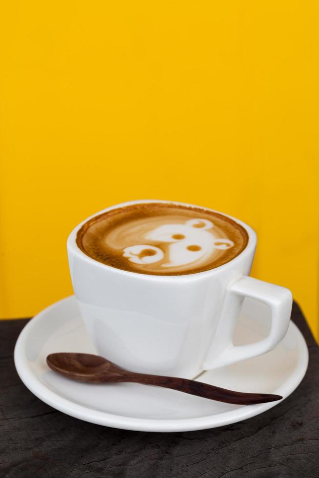xícara de café com leite como cara de urso em fundo amarelo foto