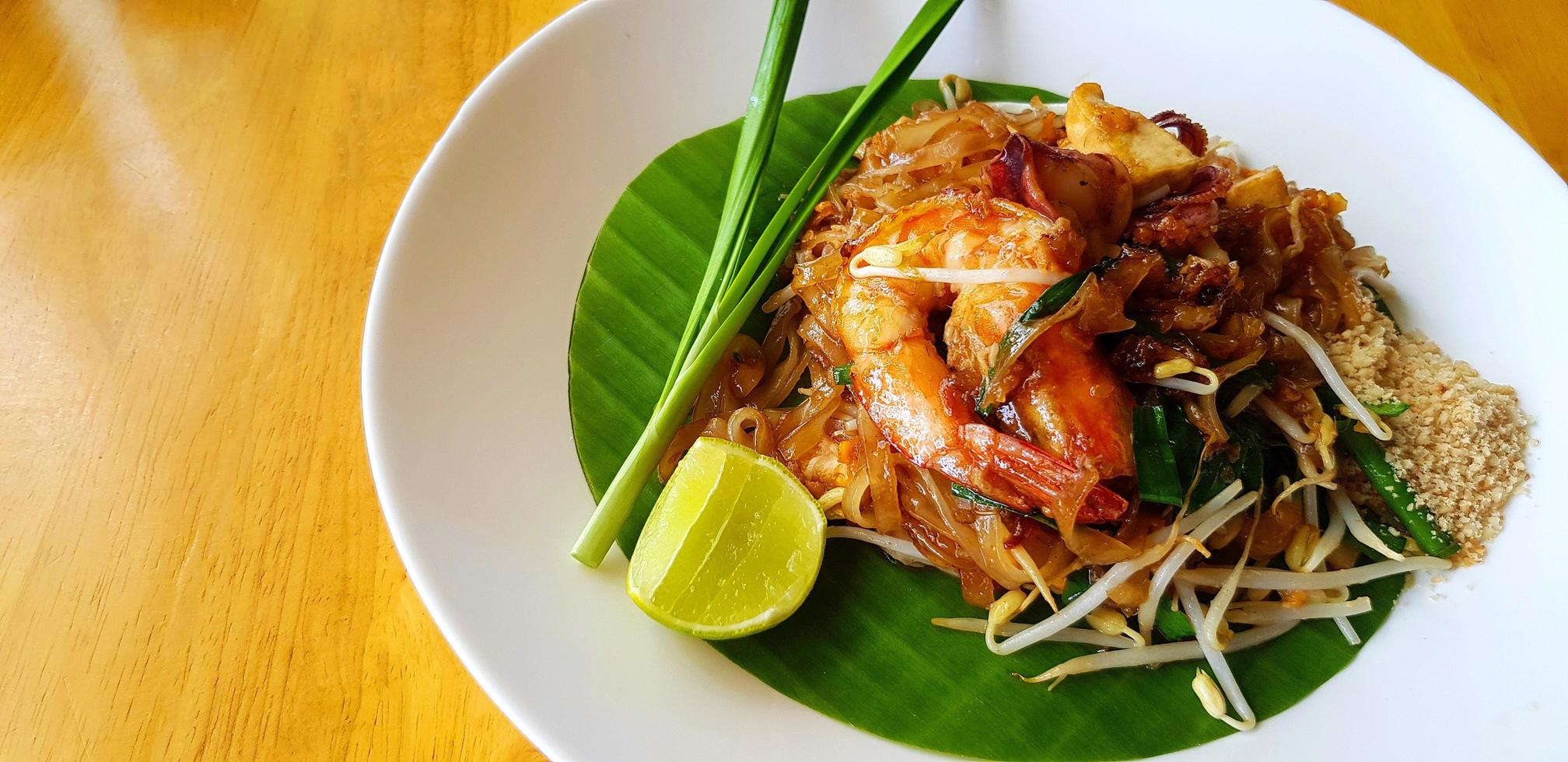 refogado com macarrão de arroz, camarão do rio ou camarão, broto de feijão, cebolinha fatiada e limão na folha de bananeira com espaço de cópia. comida famosa na tailândia call pad thai. técnica de foco seletivo. foto