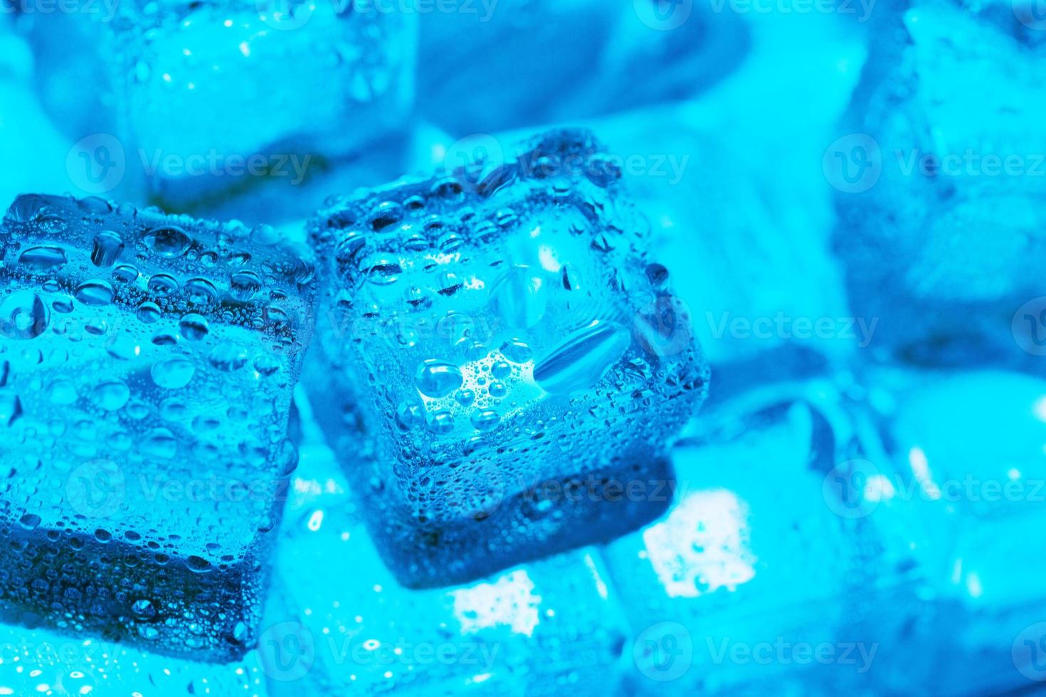 cubos de gelo com gotas de água espalhadas sobre um fundo azul, vista superior. foto