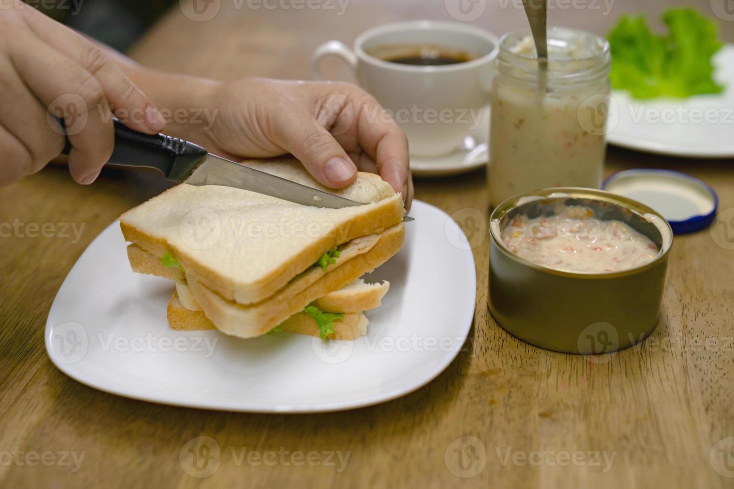 fêmea cortando um sanduíche no café da manhã com maionese de atum foto