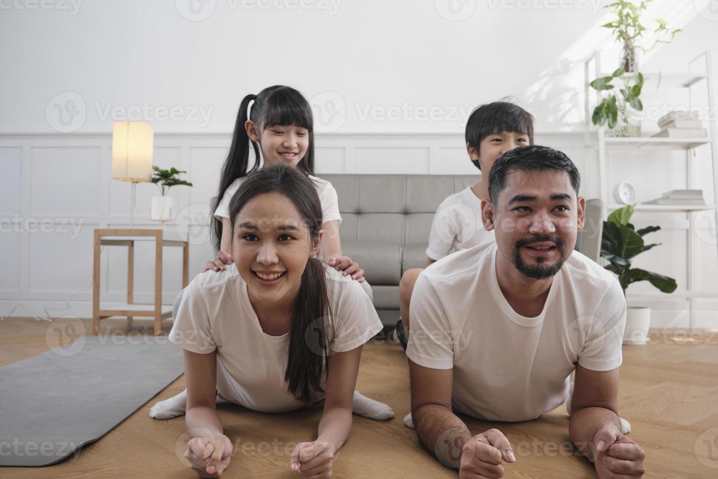 feliz bem-estar família tailandesa asiática, as crianças brincam e provocam seus pais enquanto o treinamento de ioga e a saúde se exercitam juntos na sala de estar branca, estilo de vida doméstico doméstico, atividade de fim de semana. foto