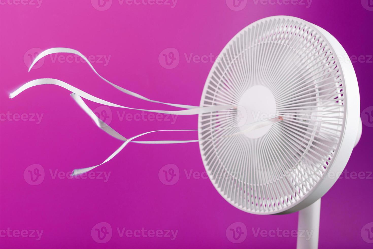 o ventilador elétrico é branco com fitas cor de rosa esvoaçando ao vento em um fundo rosa. foto