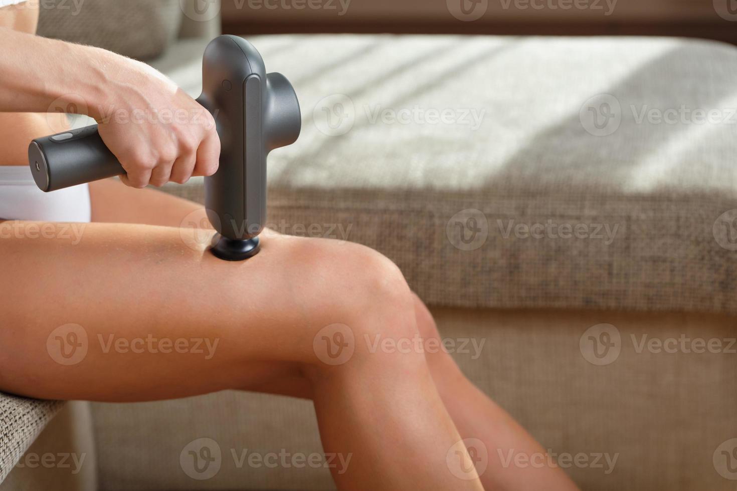 uma mulher massageia as pernas com uma pistola automática em casa. foto