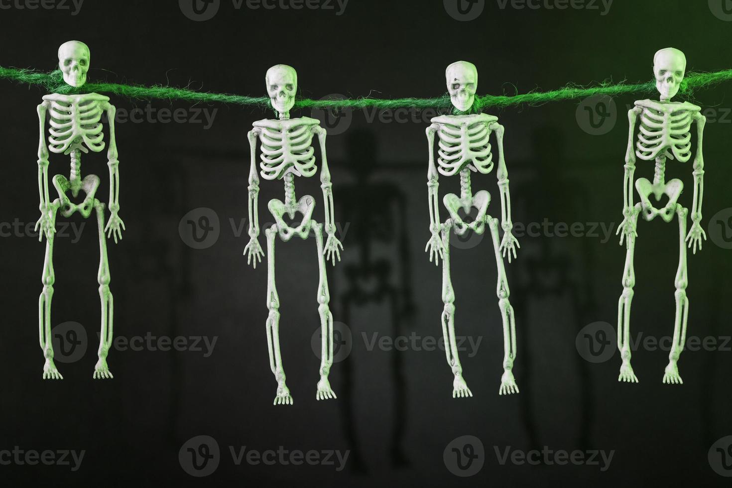 quatro esqueletos suspensos pelo pescoço em uma corda com silhuetas em um fundo escuro foto