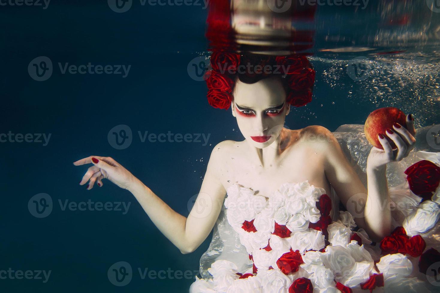 mulher de vestido feito de rosas brancas e vermelhas debaixo d'água. conto de fadas, arte, conceito de moda foto