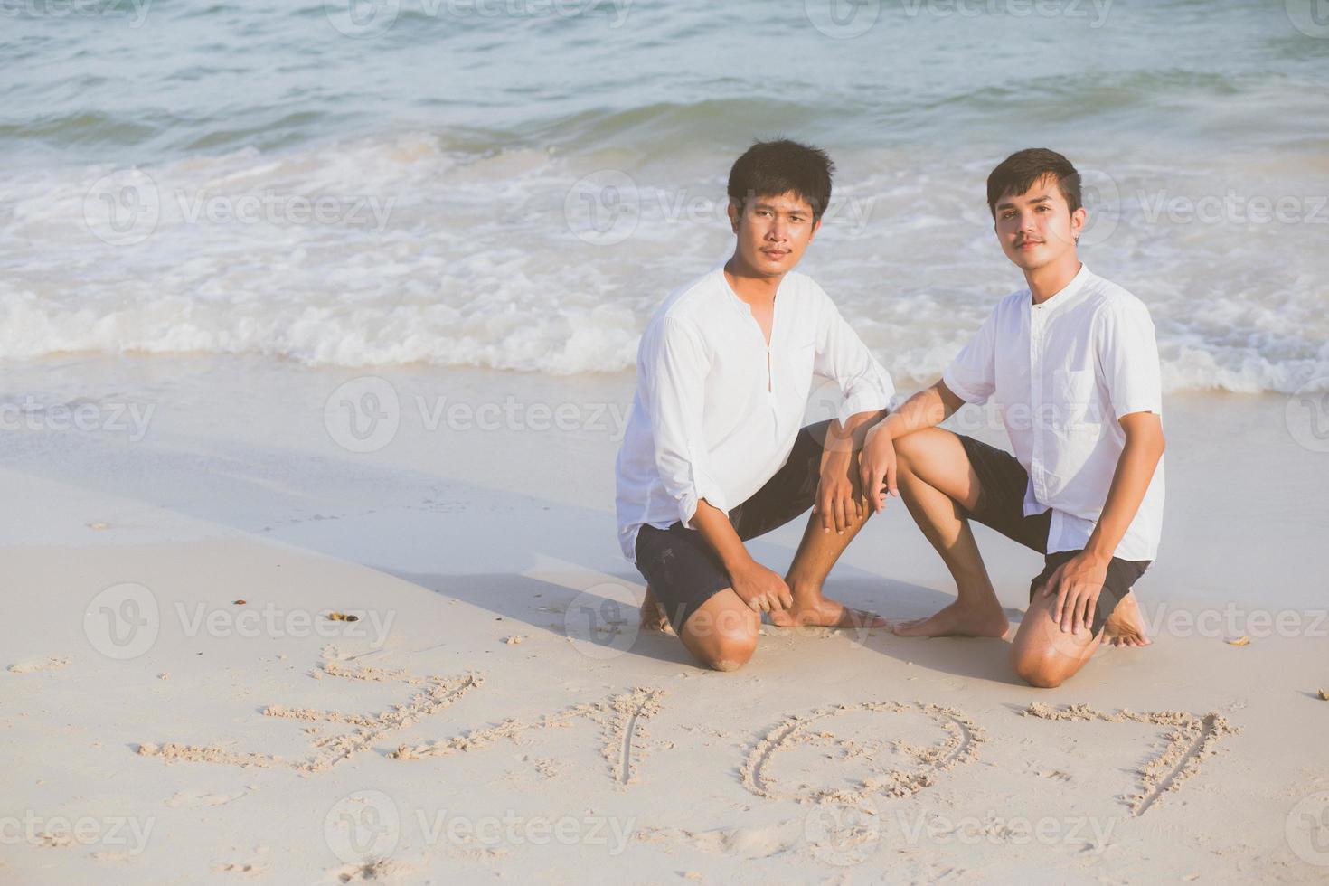 jovem casal asiático gay sorrindo romântico desenho palavra texto amor juntos na areia em férias, homossexual feliz e divertido com amor sentado na areia na praia no verão de viagens, conceito legal lgbt. foto