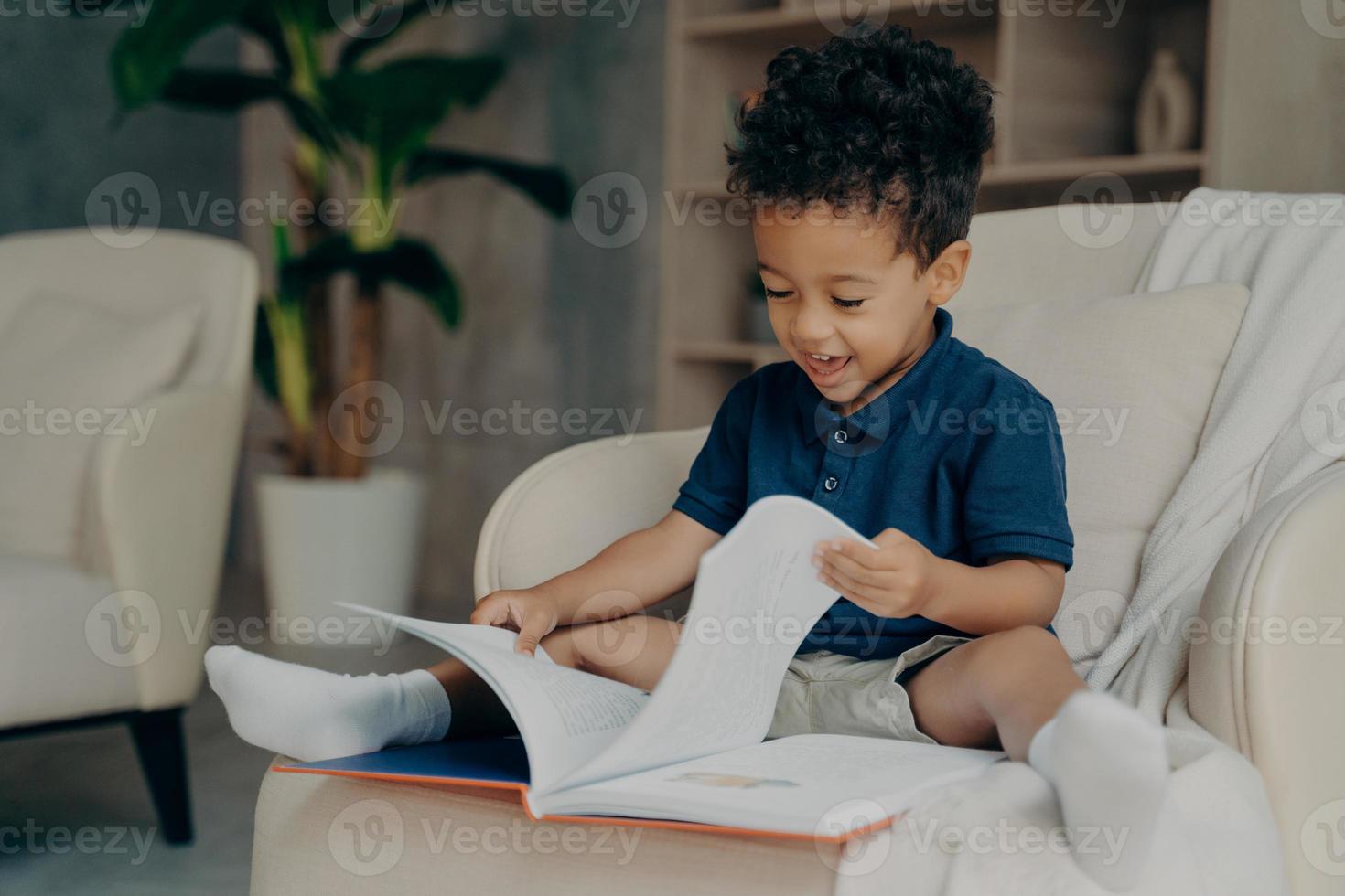 criança de raça mista feliz com cabelo encaracolado bonito lendo livro em casa foto
