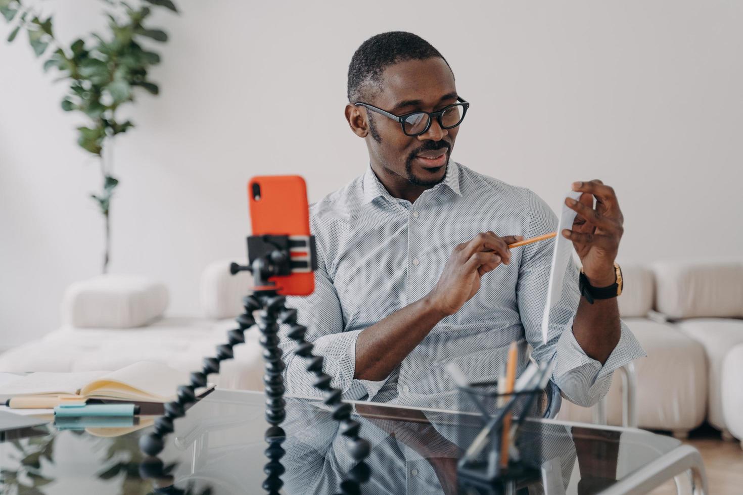 chamada de vídeo no telefone. freelancer afro tem brainstorm online. homem feliz mostra a papelada com dados. foto