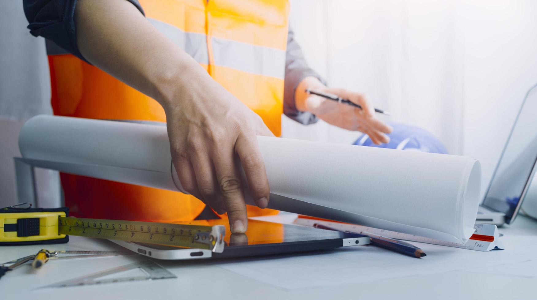 dois colegas discutindo dados de trabalho e tablet, laptop com projeto arquitetônico no canteiro de obras na mesa no escritório foto