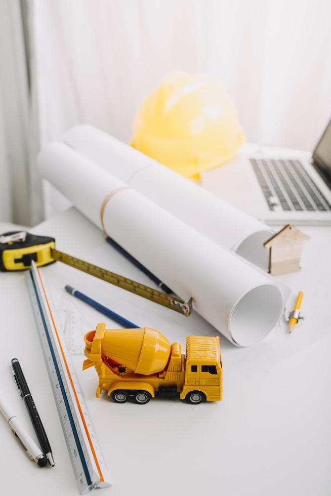 dois colegas discutindo dados de trabalho e tablet, laptop com projeto arquitetônico no canteiro de obras na mesa no escritório foto