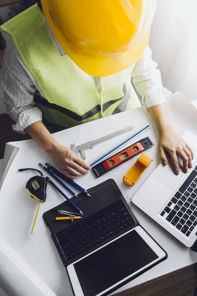 dois colegas discutindo dados de trabalho e tablet, laptop com projeto arquitetônico no canteiro de obras na mesa no escritório foto