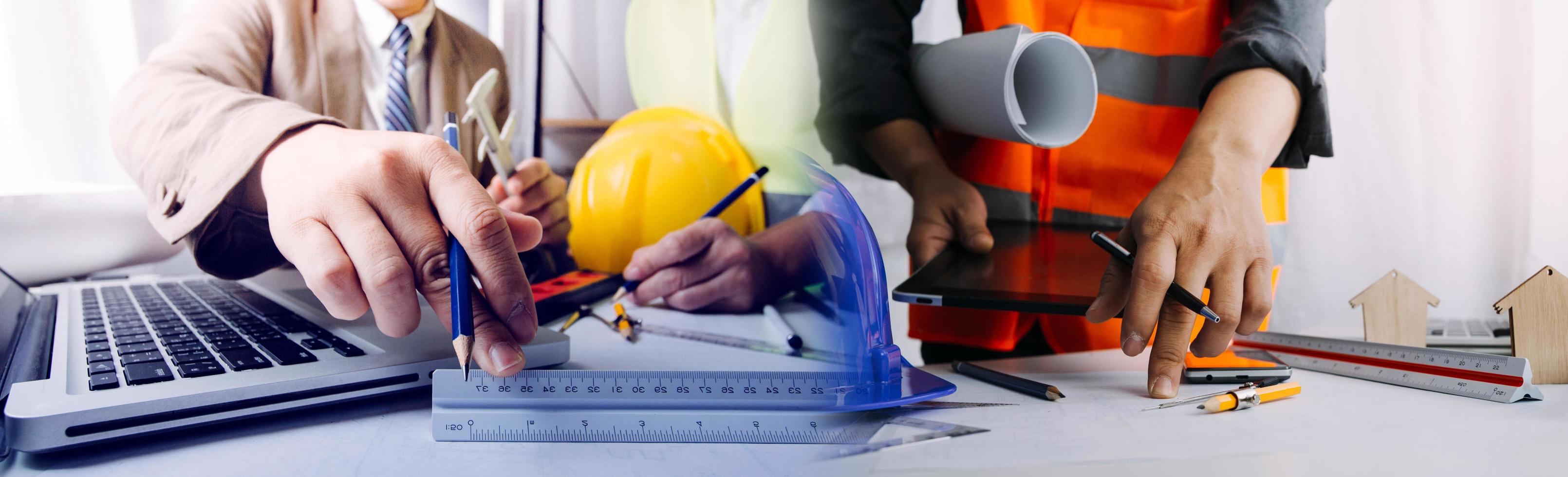 dois colegas discutindo dados de trabalho e tablet, laptop com projeto arquitetônico no canteiro de obras na mesa no escritório foto