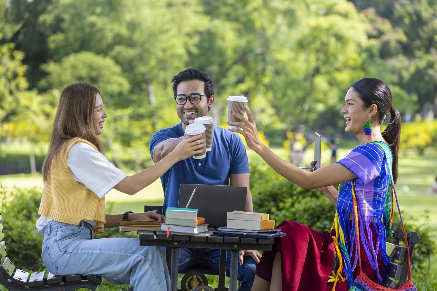 grupo de estudantes universitários está se encontrando e trabalhando em tese e projeto do lado de fora no jardim do campus universitário durante o verão enquanto torce com café quente para levar a xícara foto