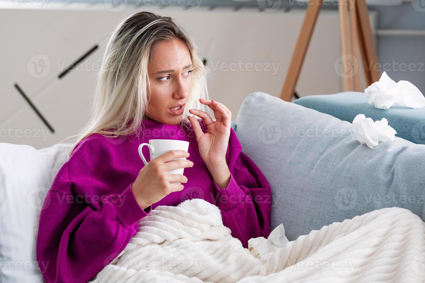 conceito de sofrer de dor terrível. linda, triste, chateada, infeliz, problemática, mulher fraca com cabelo loiro, vestindo roupas casuais está sentada em um sofá e tomando um comprimido foto