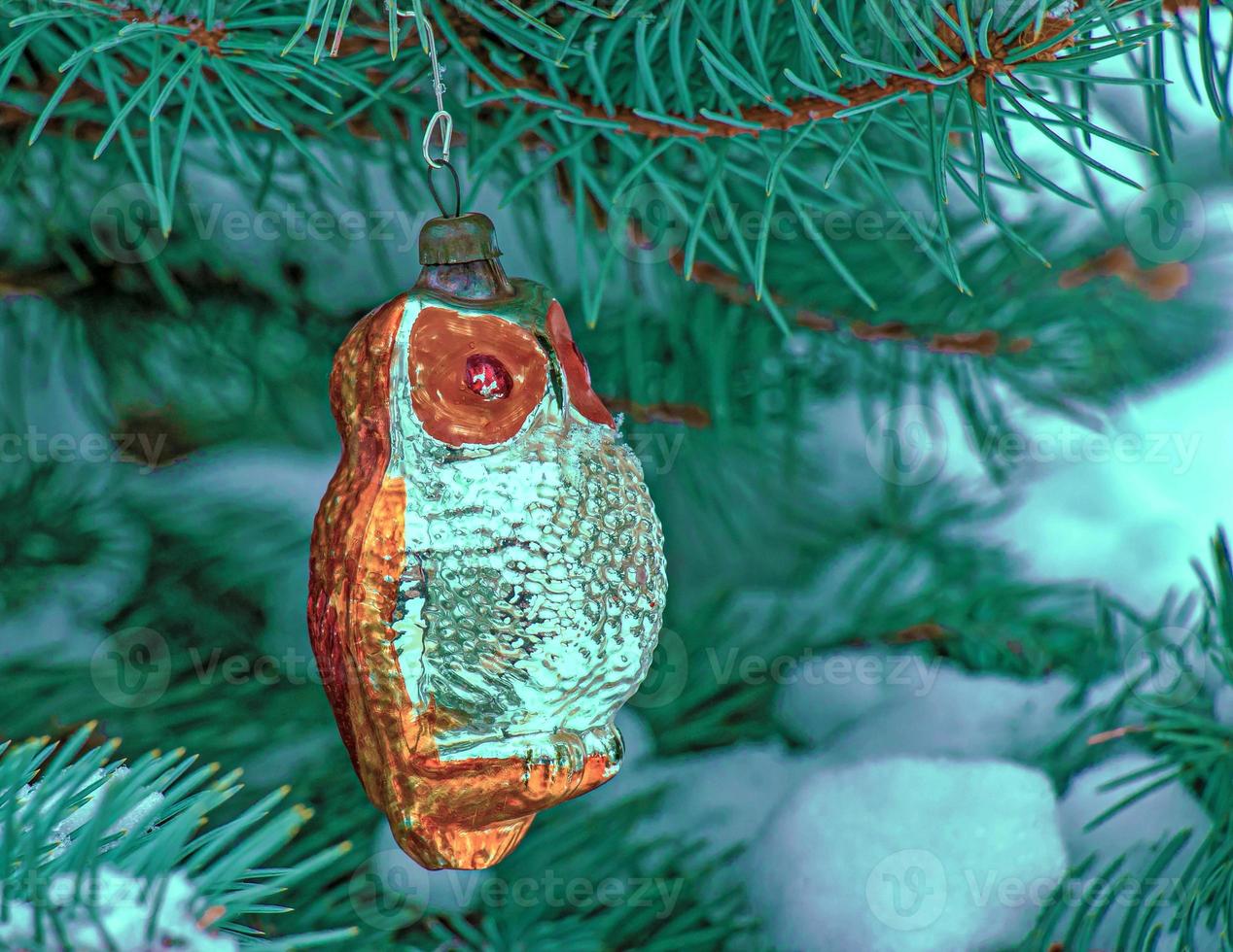 coruja de brinquedo de natal pendura em um galho coberto de neve de uma árvore de natal em um fundo festivo de bokeh de neve branca com espaço de cópia. foto