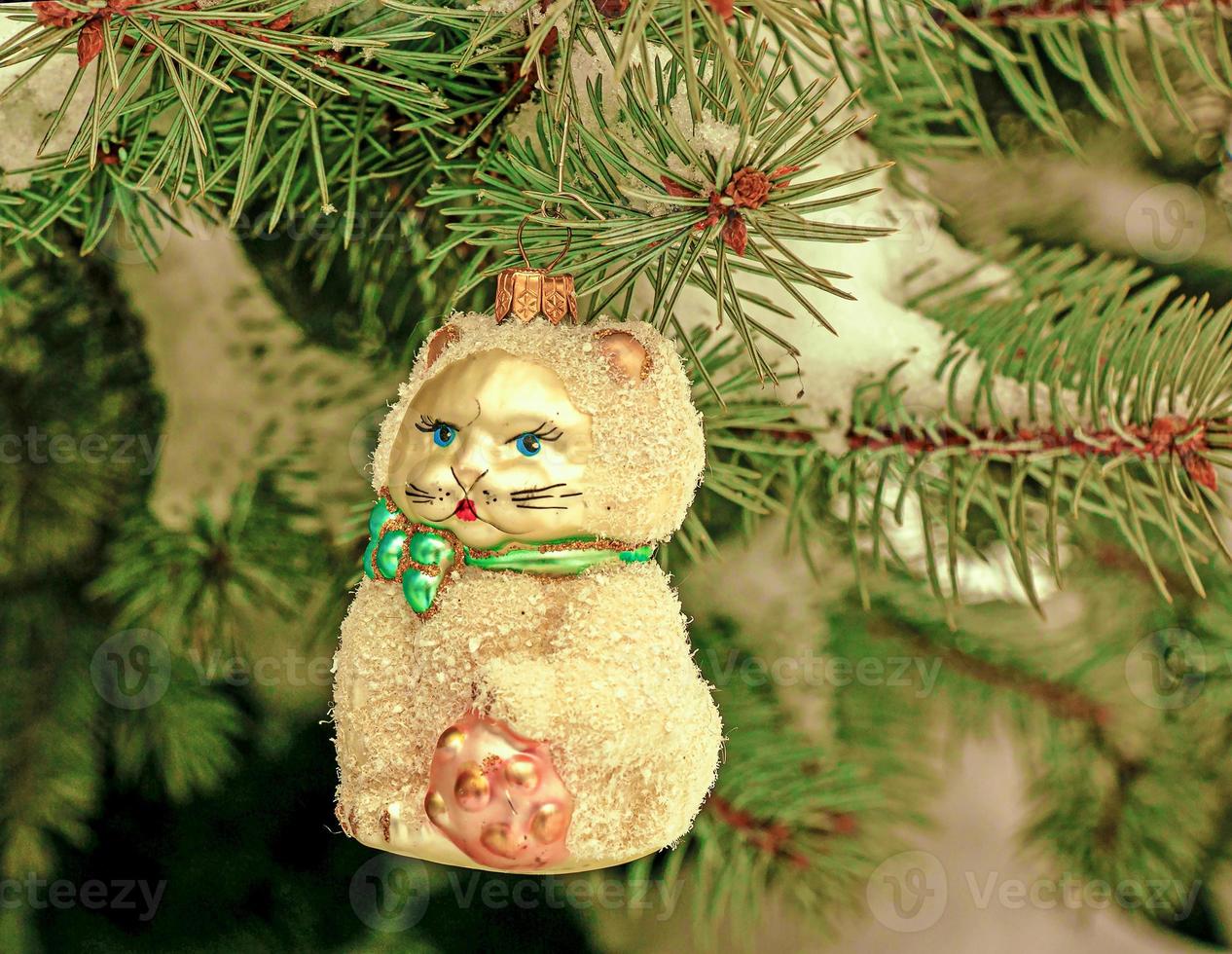 gatinho de brinquedo de natal pendura em um galho coberto de neve de uma árvore de natal em um fundo festivo de neve branca e galhos verdes de bokeh com espaço de cópia foto