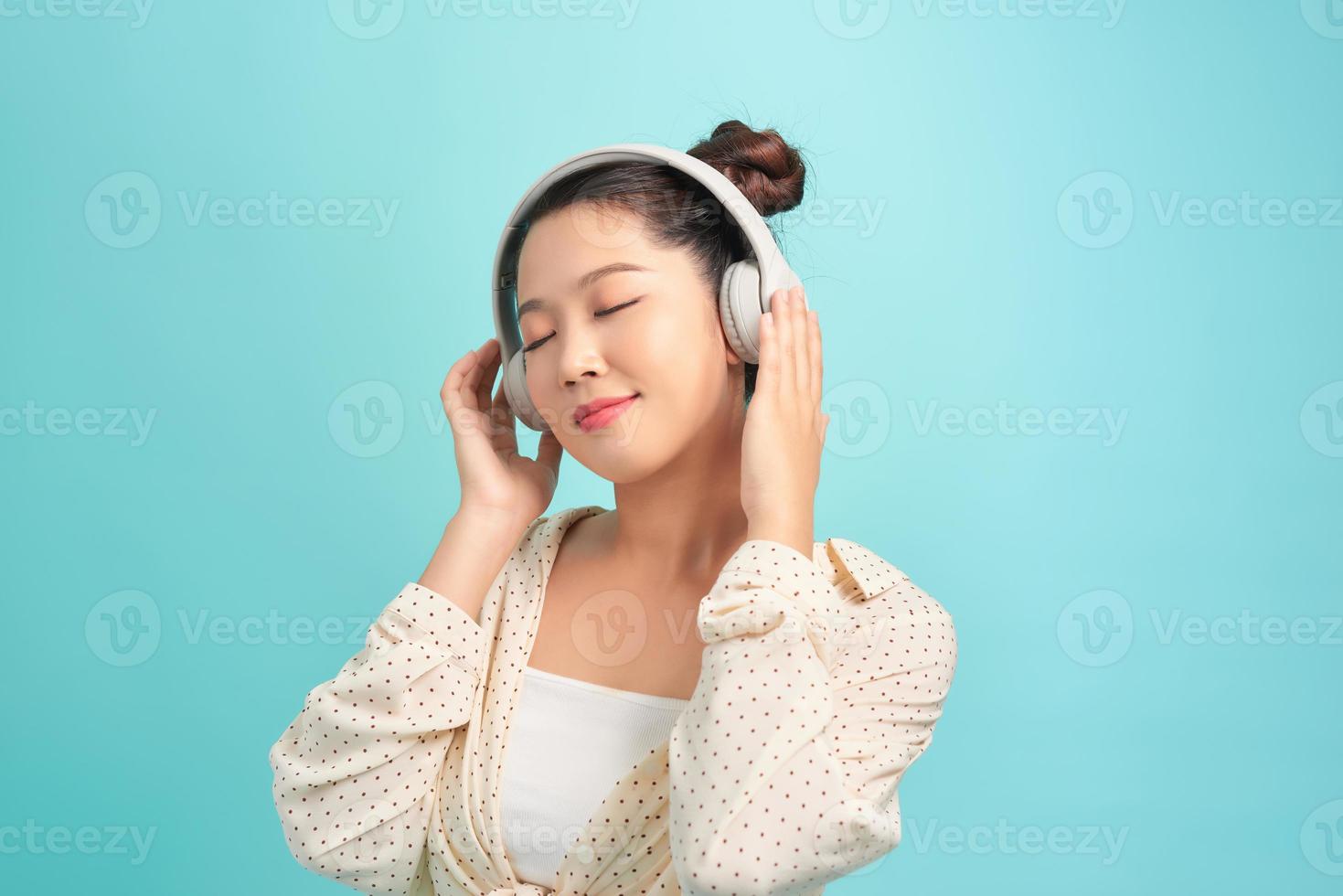 retrato de uma jovem elegante alegre em pé isolado sobre fundo azul, ouvindo música com fones de ouvido, dançando foto