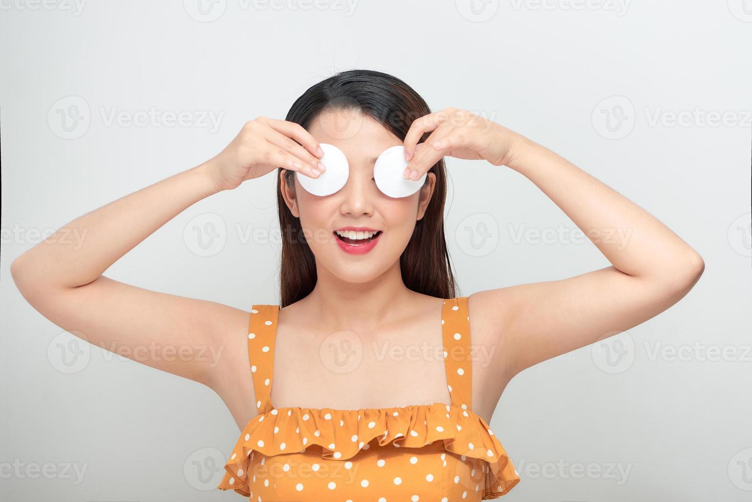 corte o rosto de limpeza feminino jovem atraente com uma almofada de algodão em um fundo branco no estúdio foto