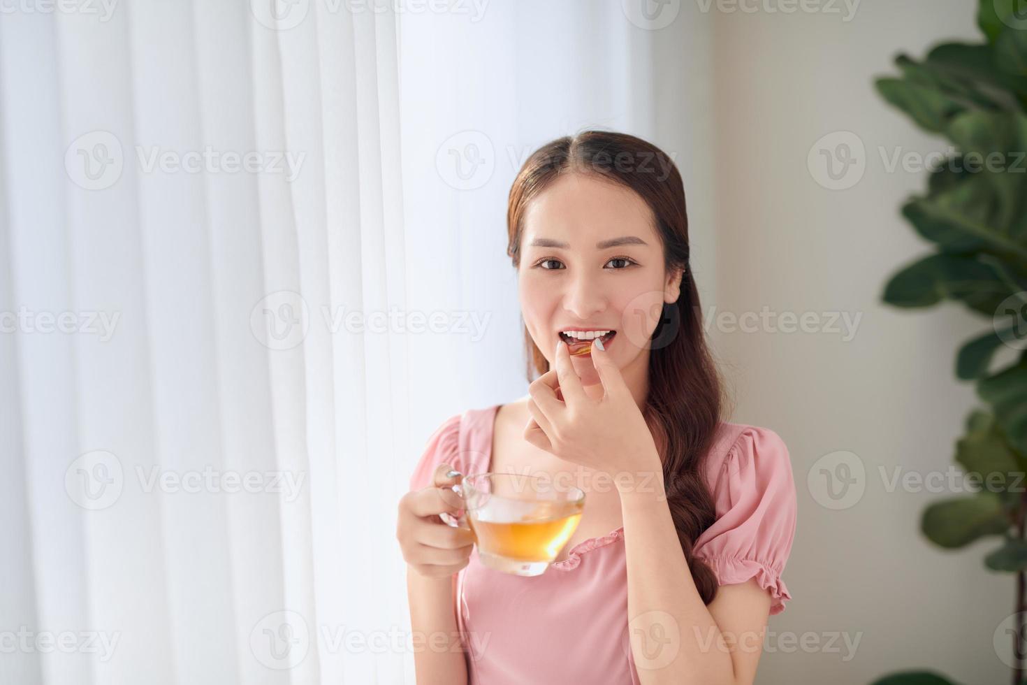 jovem e bela mulher asiática comendo pílula e água potável foto