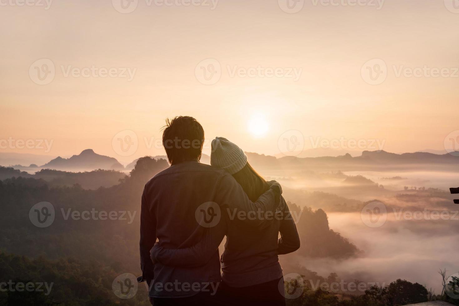 jovem casal viajante olhando para o mar de névoa e pôr do sol sobre a montanha em mae hong son, tailândia foto