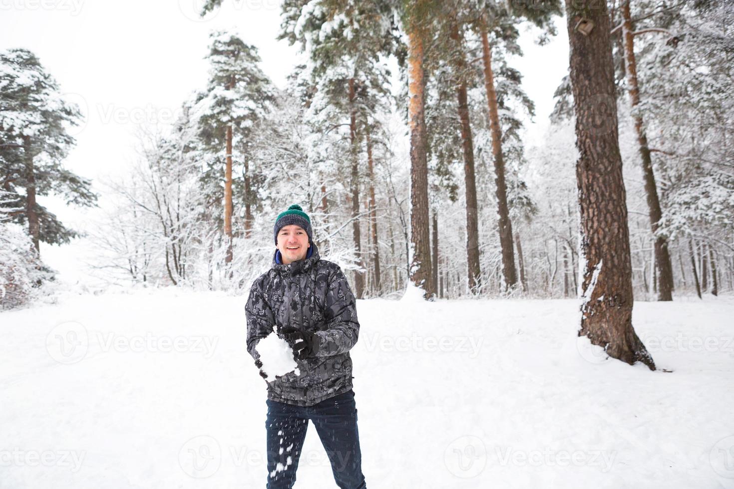 um jovem com uma bola de neve na mão está se divertindo, balançando para um lance. família de inverno e jogos amigáveis e entretenimento na floresta com neve ao ar livre foto