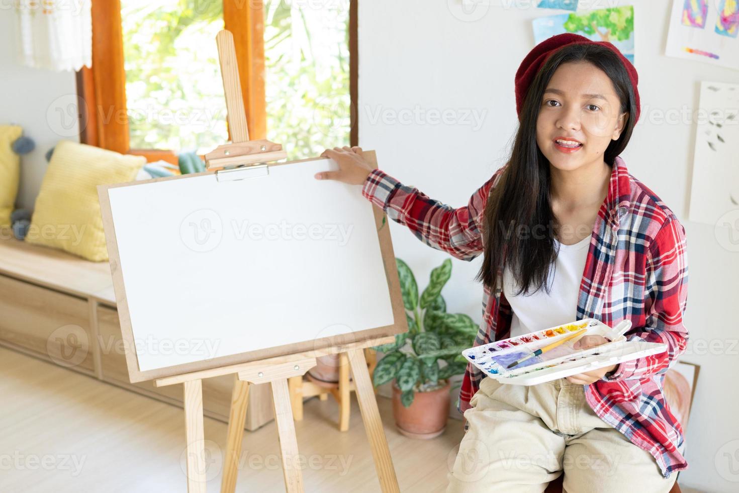 jovem sentada em uma cadeira com cavalete para desenhar segure a paleta de cores e pincel na sala. foto