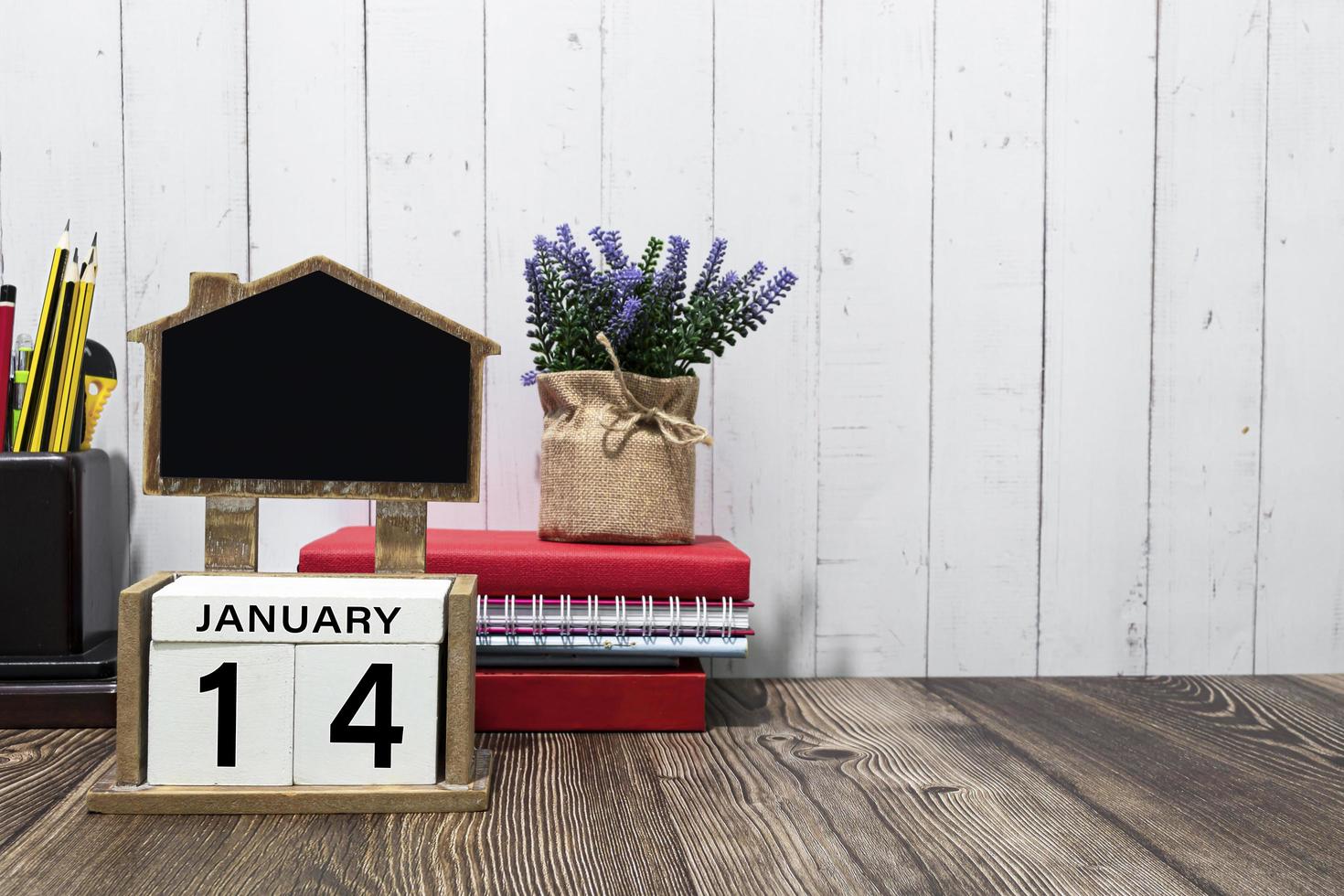 texto de data de calendário de 14 de janeiro no bloco de madeira branco com artigos de papelaria na mesa de madeira foto